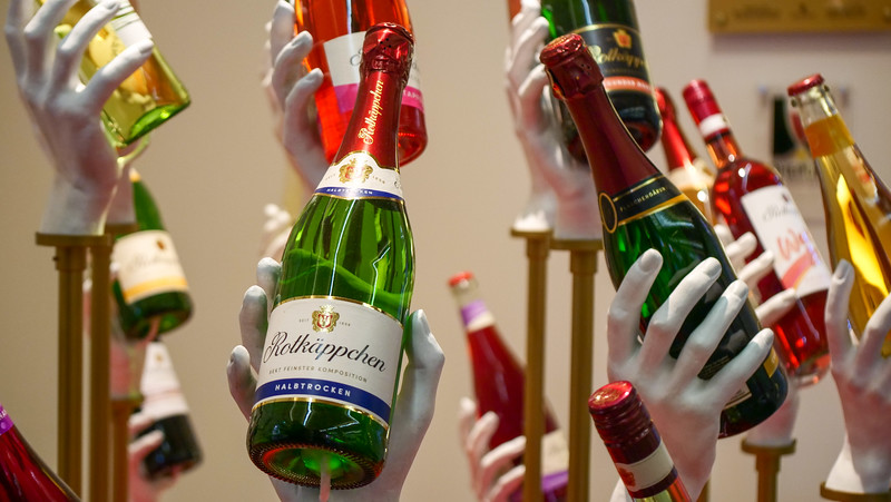 Sparkling wine art installation at Rotkäppchen-Mumm in Freyburg, Germany with individual hands holding distinct bottles of wine 