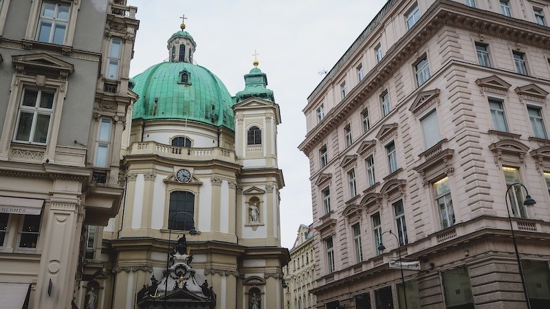 Baroque façade and green copper dome of St. Peter's Church framed by ornate historic buildings in the heart of Vienna, Austria Baroque façade and green copper dome of St. Peter's Church framed by ornate historic buildings in the heart of Vienna, Austria