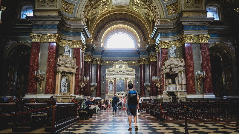 Interior of St. Stephen’s Basilica in Budapest, Hungary, showcasing its grand marble columns, ornate gold detailing, domed ceilings, and patterned floors. Visitors admire the stunning neoclassical architecture of this iconic church in the city center