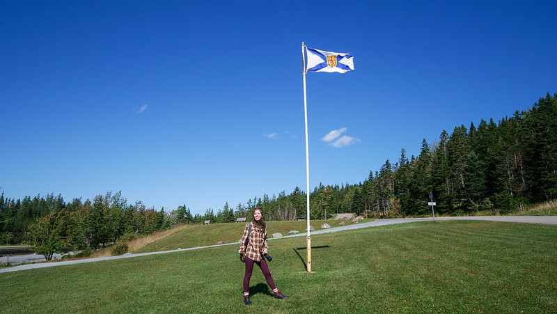 Standing next to the Nova Scotia Flag at Battery Provincial Park in St. Peters is That Backpacker Audrey Bergner on Cape Breton