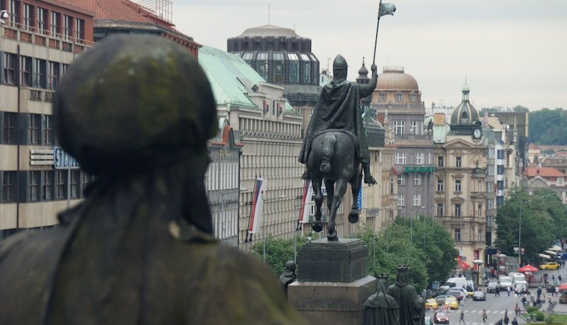 View of the equestrian Statue of Saint Wenceslas overlooking bustling Wenceslas Square in Prague, Czech Republic, framed by historic buildings and city traffic below