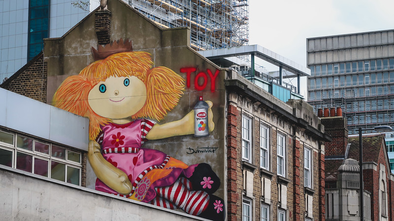 Street art in East Croydon with a giant doll carrying paint spray with the word toy spelled out visibly in London, England 