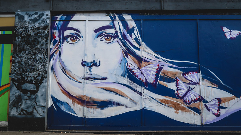 Street art in East Croydon with a lady wearing a shawl and butterflies drifting to the side in London, England 