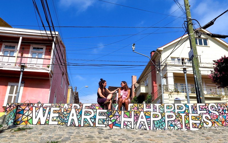 Street art in Valparaiso, Chile: We are Happies and We are hippies with colorful houses in the background 