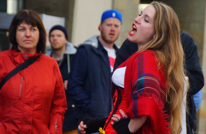 Street performer passionately singing in a vibrant red costume while entertaining passersby in Freiburg im Breisgau, Germany, during a lively outdoor show