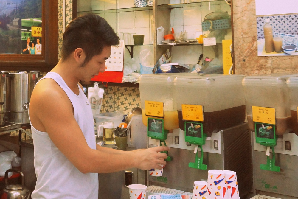 Sugar cane juice shop in Hong Kong with local man in tank-top preparing the juice in a paper cup