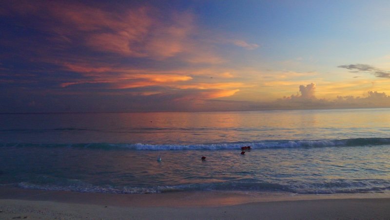 Soft pastel shades of pink, orange, and lavender spread across the sky as the sun rises over the calm turquoise waters of Cayo Santa María, Cuba, casting a tranquil glow on the gentle waves and sandy shoreline during a romantic honeymoon morning