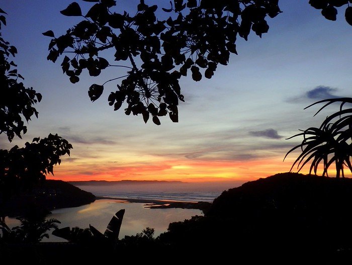 Sunrise in Cintsa, South Africa with silhouette foliage and trees framing coastal views and fiery clouds for an incredible natural scenery from a high vantage point