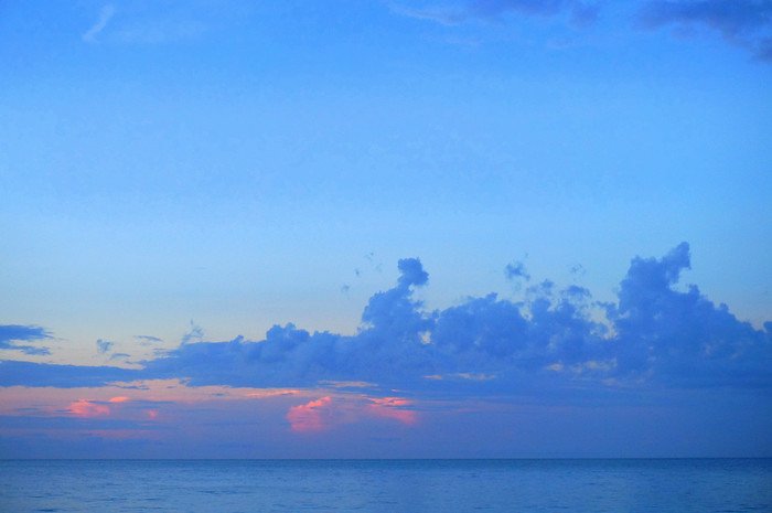 Soft pastel hues of pink and orange glow beneath scattered clouds as the sun sets over the calm Caribbean Sea, painting the sky in tranquil shades of blue along the beaches of Cayo Santa María, Cuba during a romantic honeymoon evening