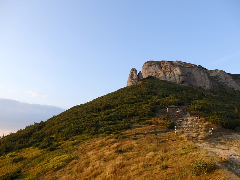 Sunset hike in Romania with views of the top of the mountain and a building that is dwarfed by its sheer size in comparison 
