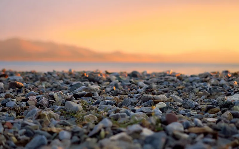 Sunset on Song Kol Lake with macro views of rocks and pebbles in the foreground and blurred mountain range and lake in the background