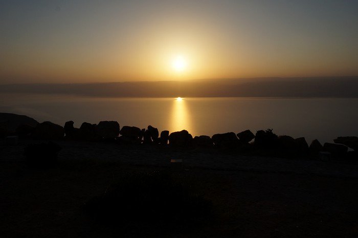 Sunset over the Dead Sea in Jordan with a golden orb and golden rays shining over a silhouette 