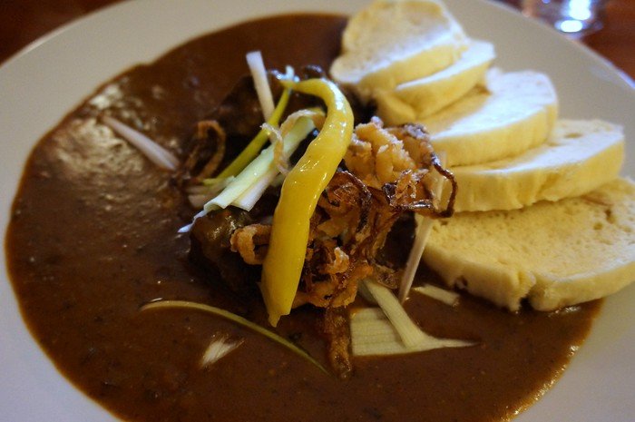 Traditional Czech Svíčková dish served in Prague, Czech Republic, featuring tender beef in creamy vegetable sauce with bread dumplings, crispy fried onions, and pickled pepper garnish