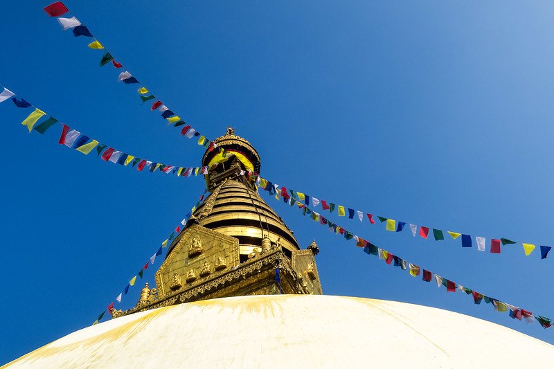 Golden stupa of Swayambhunath Monkey Temple in Kathmandu draped with colorful Buddhist prayer flags under a clear blue sky, a spiritual highlight for visitors exploring Nepal’s sacred heritage sites