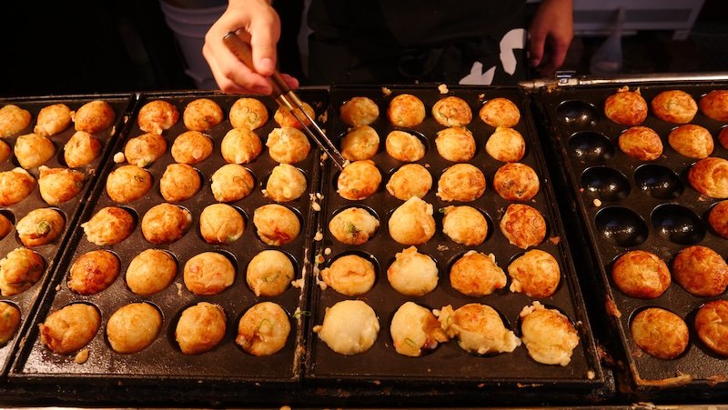 Takoyaki being prepared and flipped before our eyes as the ultimate street food in Osaka, Japan 