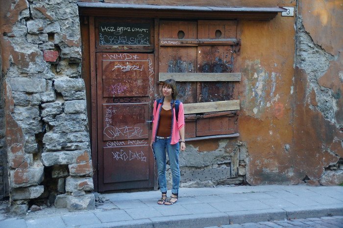 That Backpacker Audrey Bergner standing in front of crumbling stone walls and boarded-up wooden doors covered in graffiti in Tallinn, Estonia during a day trip from Helsinki