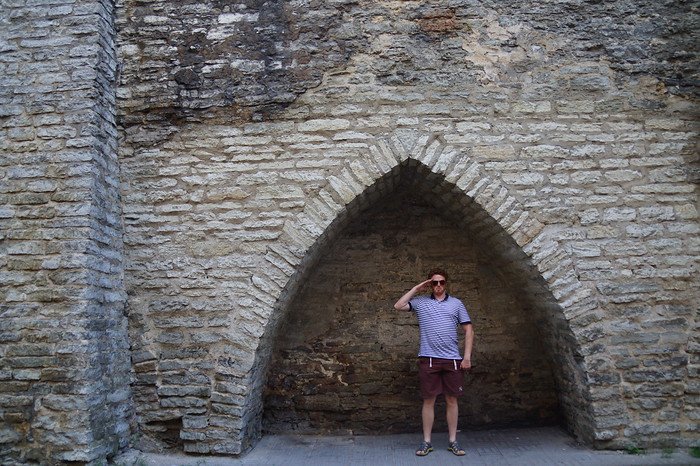 Nomadic Samuel posing playfully under a medieval stone archway in Tallinn, Estonia during a day trip from Helsinki, Finland