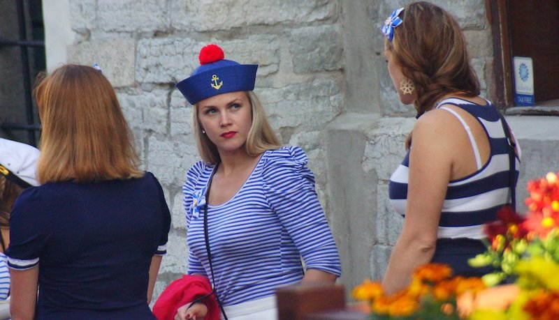 Women in nautical striped outfits at a cultural street festival in Tallinn, Estonia during a summer day trip from Helsinki