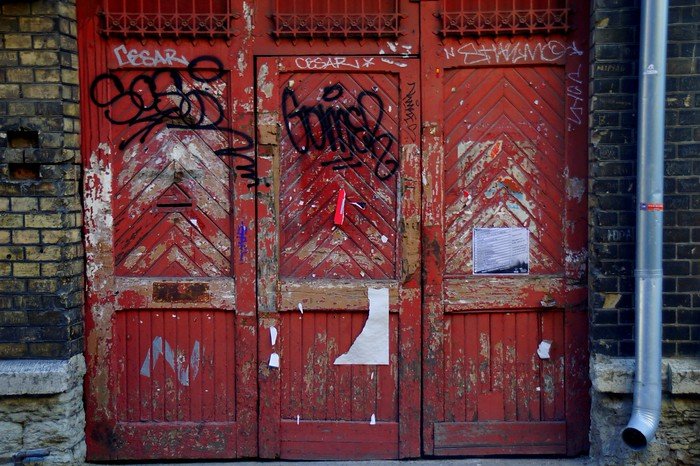 Weathered red wooden doors covered in graffiti tags and peeling paint in Tallinn, Estonia, showcasing the city’s urban street art scene