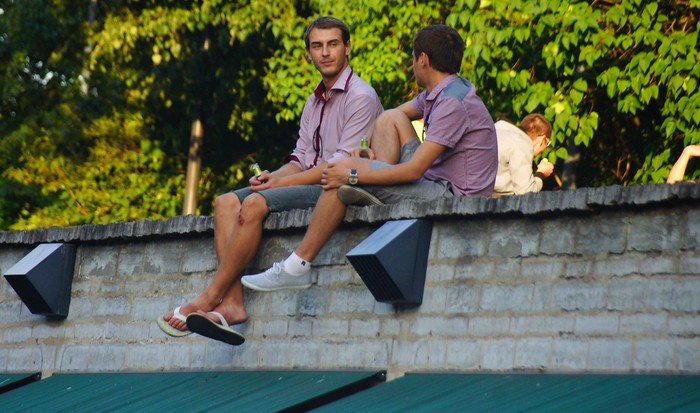 Young men enjoying beer while sitting on a rooftop overlooking a busy street in Tallinn, Estonia during a summer day trip from Helsinki