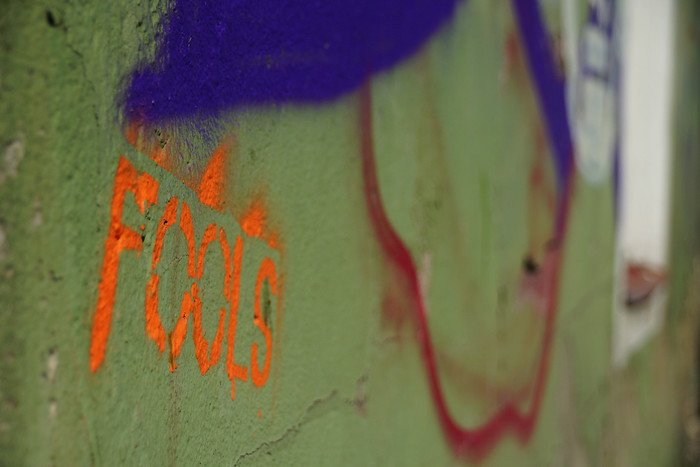 Street art stencil with the word ‘Fools’ painted in orange on a green wall in Tallinn, Estonia, highlighting the city’s urban graffiti culture