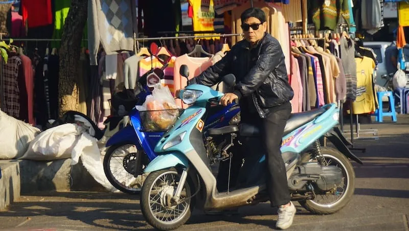 Thai man with a leather jacket and sunglasses riding a scooter in Chiang Mai, Thailand 