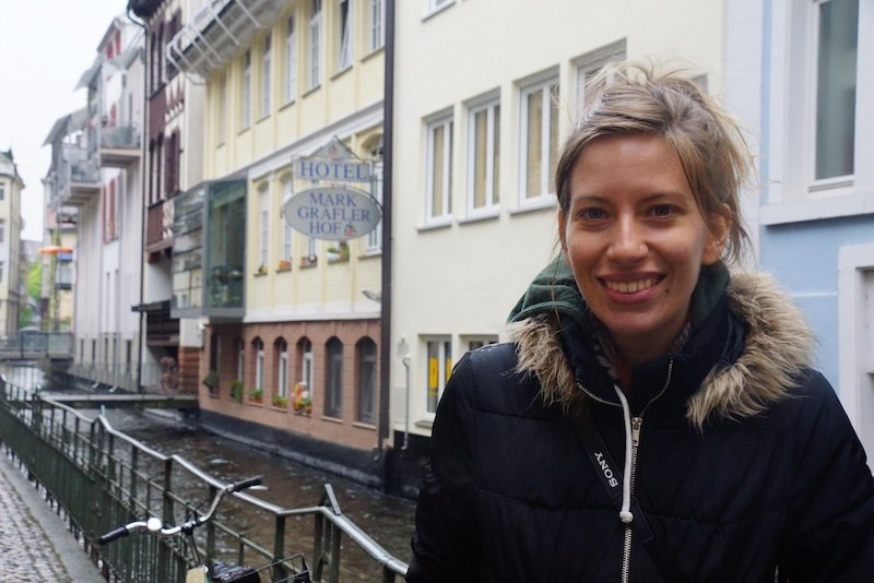 That Backpacker Audrey Bergner standing beside a scenic Bächle canal lined with colourful historic buildings in Freiburg im Breisgau, Germany, on a misty morning walk
