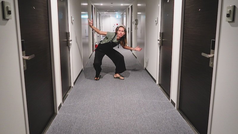 Audrey Bergner of That Backpacker playfully posing in the hallway of a modern business hotel during her stay in Nikko, Japan, surrounded by sleek white walls and dark wooden doors