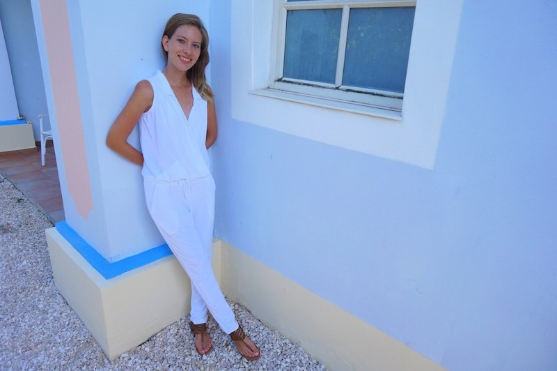 That Backpacker Audrey Bergner posing in a chic white jumpsuit against pastel walls in Cuba, showcasing comfortable yet stylish honeymoon clothing for tropical travel