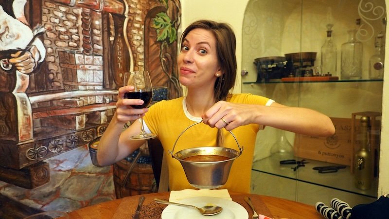 That Backpacker Audrey Bergner excited to be holding a pot of goulash and a glass of red wine in Budapest, Hungary 