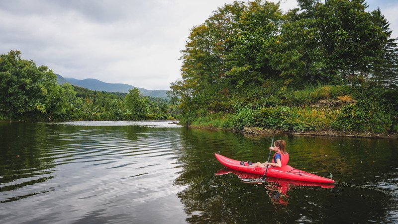 That Backpacker Audrey Bergner kayaking along the tranquil Missisquoi River surrounded by lush greenery and rolling hills at Au Diable Vert in Sutton, Quebec, during an outdoor adventure in the Eastern Townships