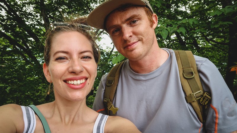 Nomadic Samuel and Audrey Bergner of That Backpacker smiling for a selfie during their trip to Nikko, Japan, surrounded by lush green forest on a warm summer day