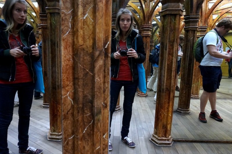 That Backpacker Audrey Bergner exploring the historic Mirror Maze at Petřín Hill in Prague, Czech Republic, surrounded by reflections in ornate wooden-framed mirrors