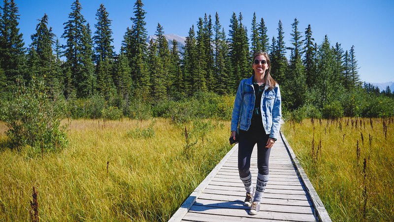 Audrey Bergner from That Backpacker walking along the wooden Policeman's Creek Boardwalk surrounded by golden marsh grasses and tall evergreens in Canmore during our Canadian Rockies road trip