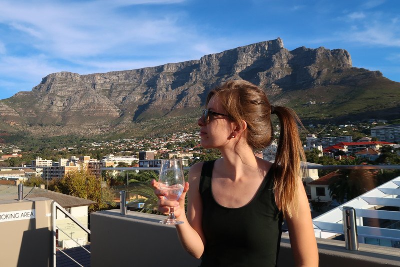 Audrey Bergner from That Backpacker enjoying a glass of wine on a rooftop terrace with sweeping views of Table Mountain and the cityscape of Cape Town under a bright blue sky