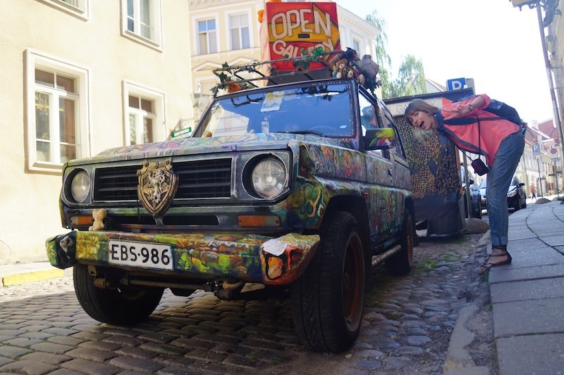 That Backpacker Audrey Bergner posing playfully beside a colorful street art car in Tallinn, Estonia during a day trip from Helsinki