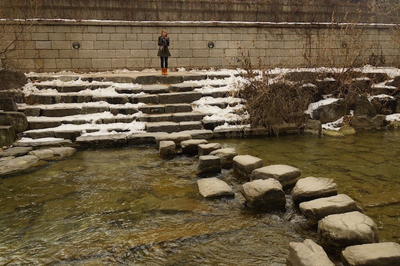 That Backpacker Audrey Bergner taking photos oft he Cheonggyecheong stream river in Seoul during winter with snow 