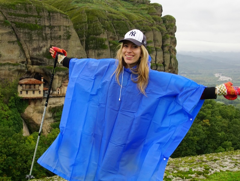 That Backpacker Audrey Bergner wearing a rain poncho, hat and hiking poles highlighting the ever changing weather in Meteora, Greece 