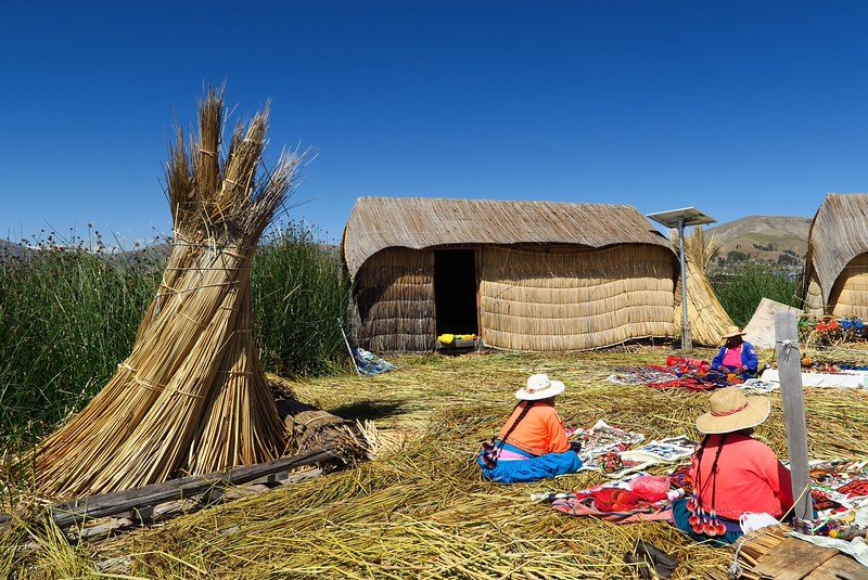 The floating reed islands of Uros located on Lake Titicaca with local ladies dressed in bright colors wearing sun hats and selling crafts in Peru