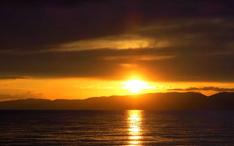 The sun setting in Song Kol Lake over the mountain range with a beam of light glowing over the lake in Kyrgyzstan