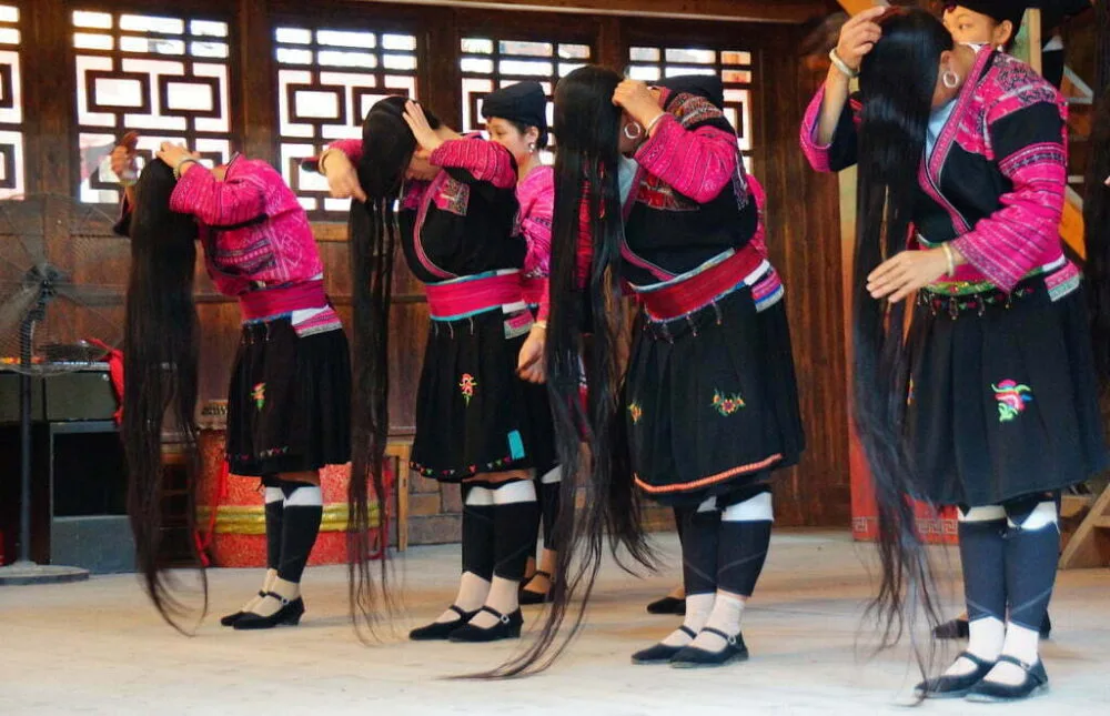 The Women With The Longest Hair In China showing us the complete length of their hair by putting in front of their faces and bending down