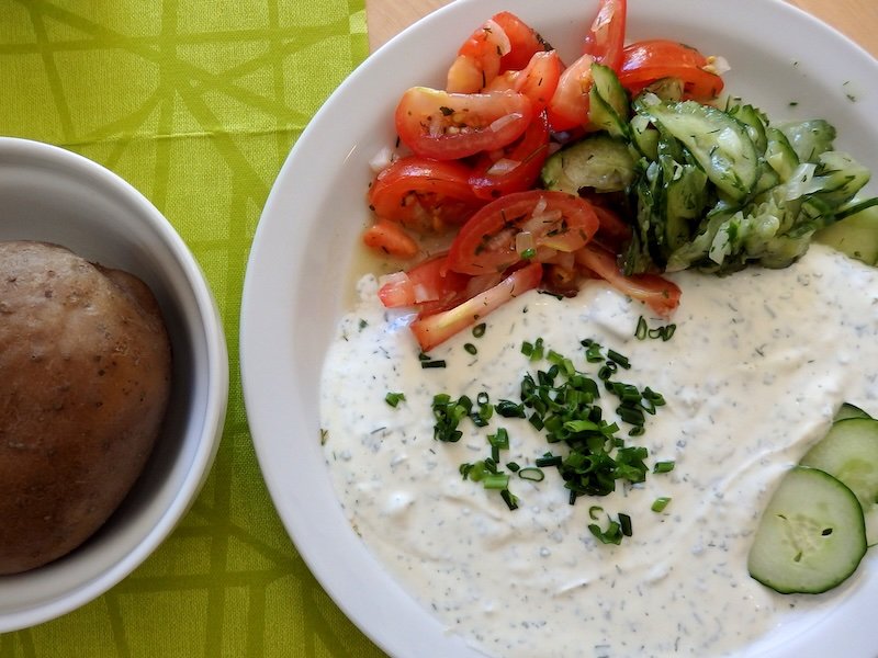 Traditional Quark mit Leinöl dish from Germany served on Rügen Island, featuring boiled potatoes, creamy herbed quark topped with chopped chives, and sides of fresh cucumber and tomato salad for a light summer meal