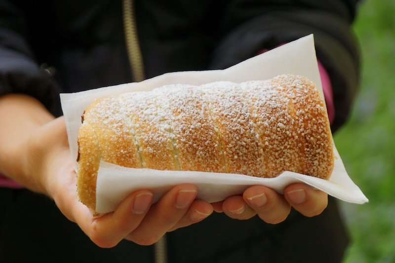 Hands holding a freshly baked Trdelník chimney cake dusted with powdered sugar, a popular street food treat in Prague, Czech Republic