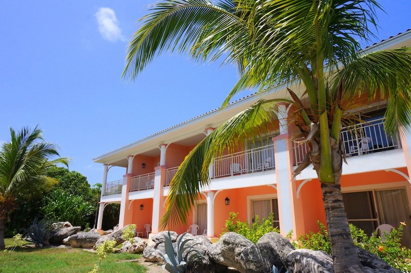 A vibrant peach-coloured resort building framed by swaying palm trees and lush tropical landscaping under a brilliant blue sky at Cayo Santa María, Cuba, capturing the serene and sunny atmosphere of a romantic Caribbean honeymoon stay