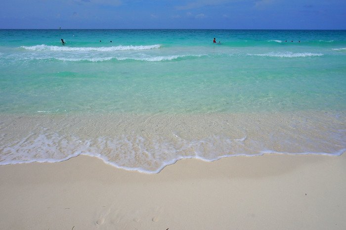 Gentle turquoise waves lap against the soft white sand on a sunny tropical beach in Cayo Santa María, Cuba, showcasing the island’s crystal-clear waters and inviting shoreline during a romantic honeymoon escape