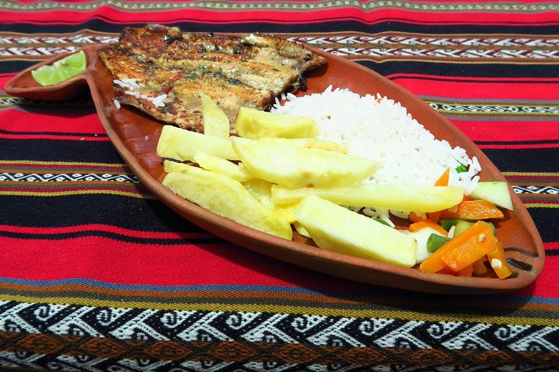 Trout lunch in Taquile with large cut potato fries and rice along with vegetables on a uniquely shaped plate that looks like a boat 