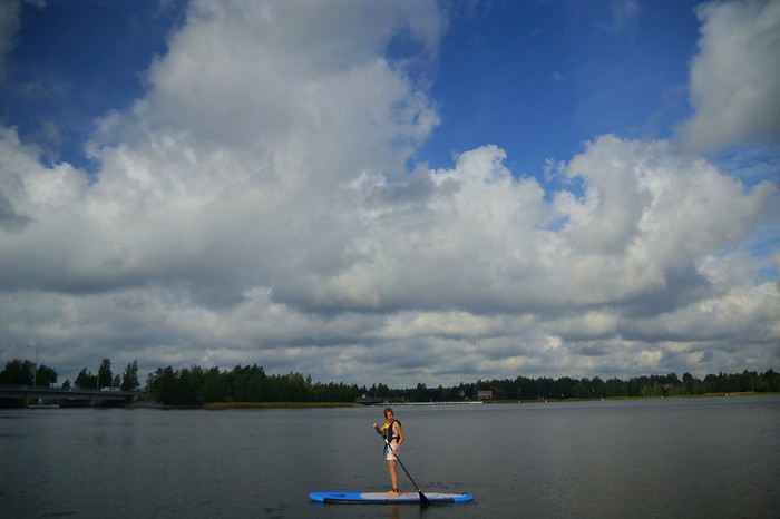 Trying paddleboarding for the first time in Finland That Backpacker Audrey out on the water with fluffy white clouds in the background