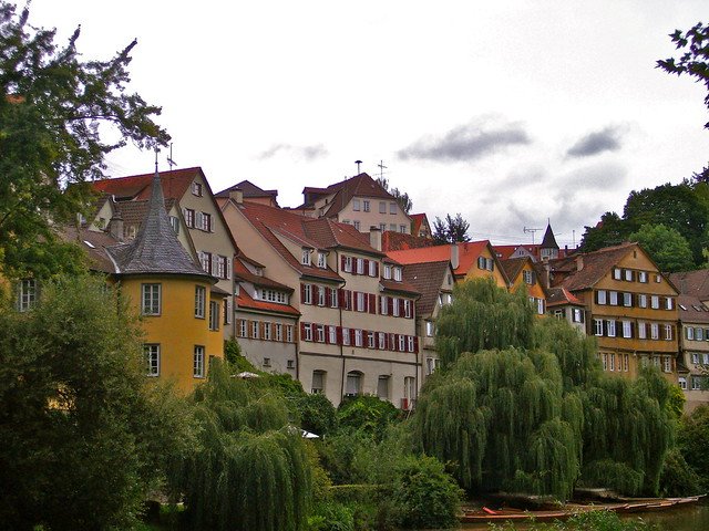 Scenic view of Tübingen, Germany, with colorful historic houses along the Neckar River, red-tiled rooftops, willow trees overhanging the water, and traditional wooden punts, capturing the charm of this university town
