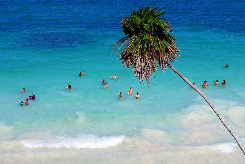 Travelers swimming in the turquoise Caribbean waters at the beach below the Mayan ruins of Tulum near Playa del Carmen, Mexico