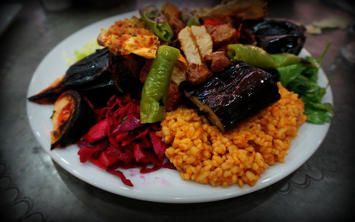 A vibrant Turkish feast in Istanbul, Turkey featuring grilled eggplant, juicy kebab meat, stuffed vegetables, pickled red cabbage, green peppers, and a side of fluffy bulgur pilaf on a white plate